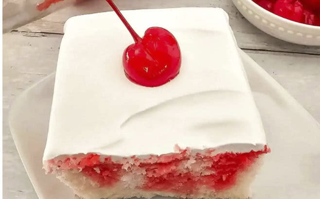 A square slice of white cake with a red cherry on top, covered in white frosting, sits on a white plate—the perfect sweet touch to end any backyard barbecue.